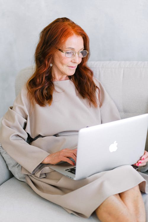 Aged businesswoman in eyeglasses typing important report on laptop