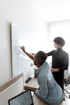 Two men brainstorming and collaborating at a whiteboard in a modern office setting.
