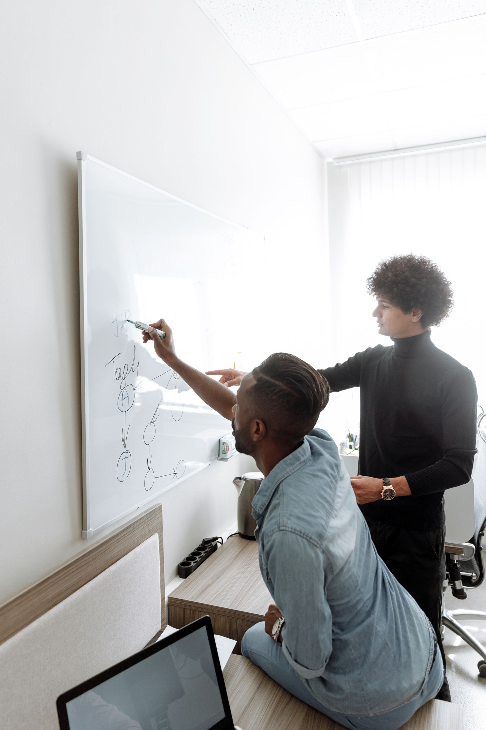 Two people planning at a whiteboard in a bright office