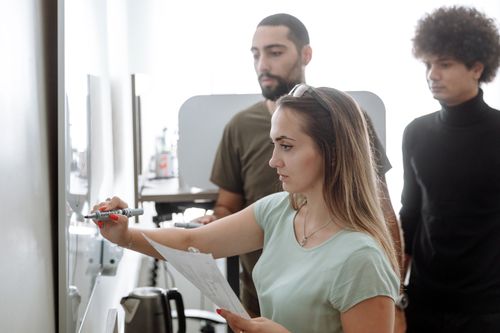 Free Three young professionals brainstorming on a whiteboard in a modern office setting. Stock Photo
