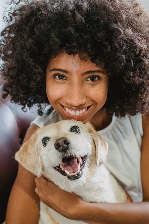 Cheerful African American female cuddling adorable puppy while smiling and looking at camera
