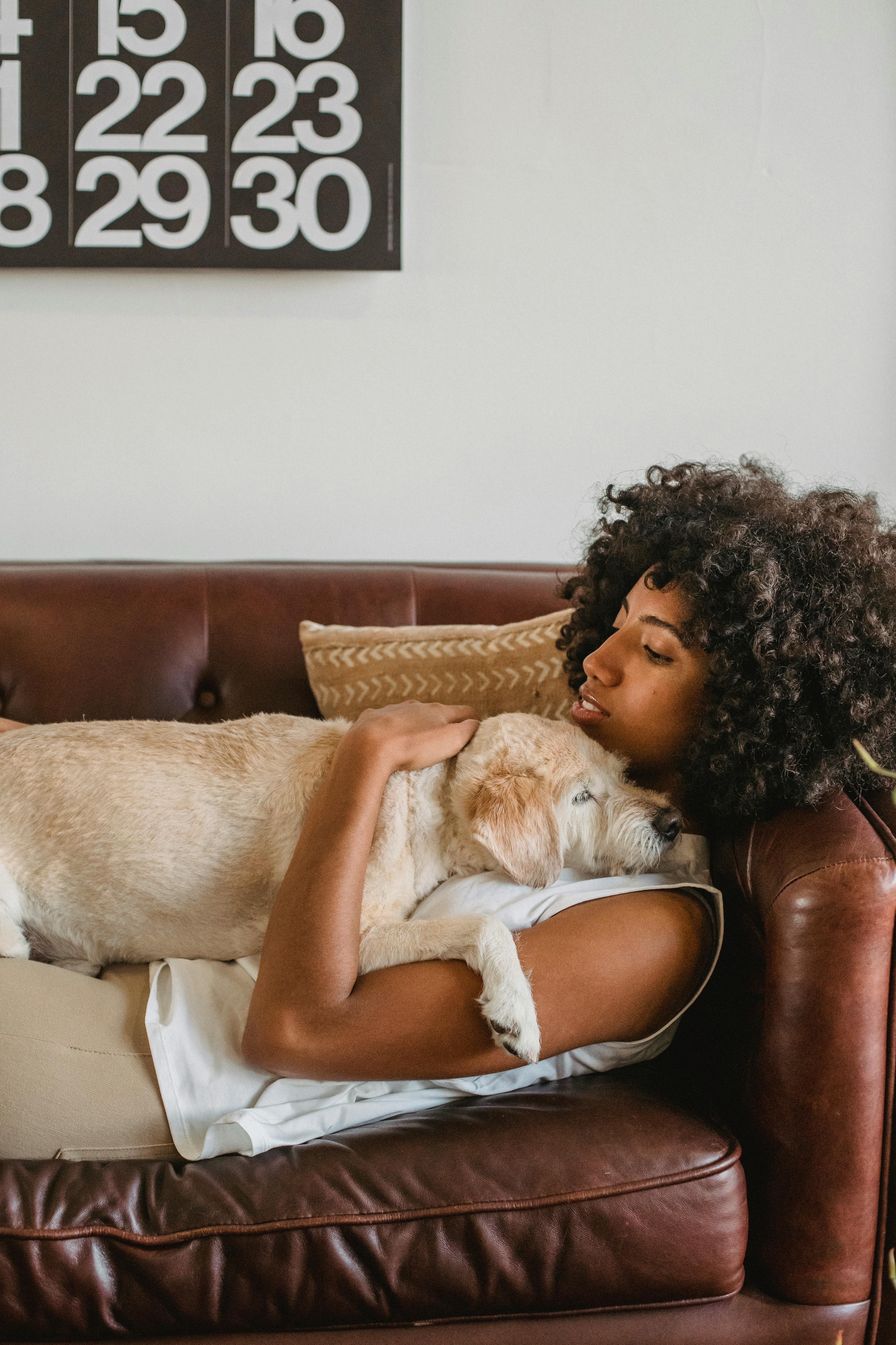 Woman Lying Down on Brown Leather Couch With Her Dog