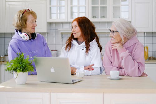 Positive senior women standing at table in kitchen and communicating