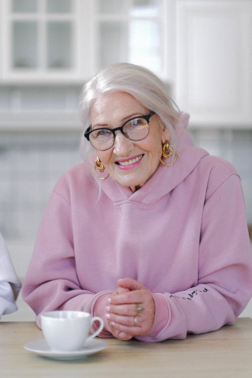 Free Smiling aged woman in hoodie sitting at table in light apartment Stock Photo