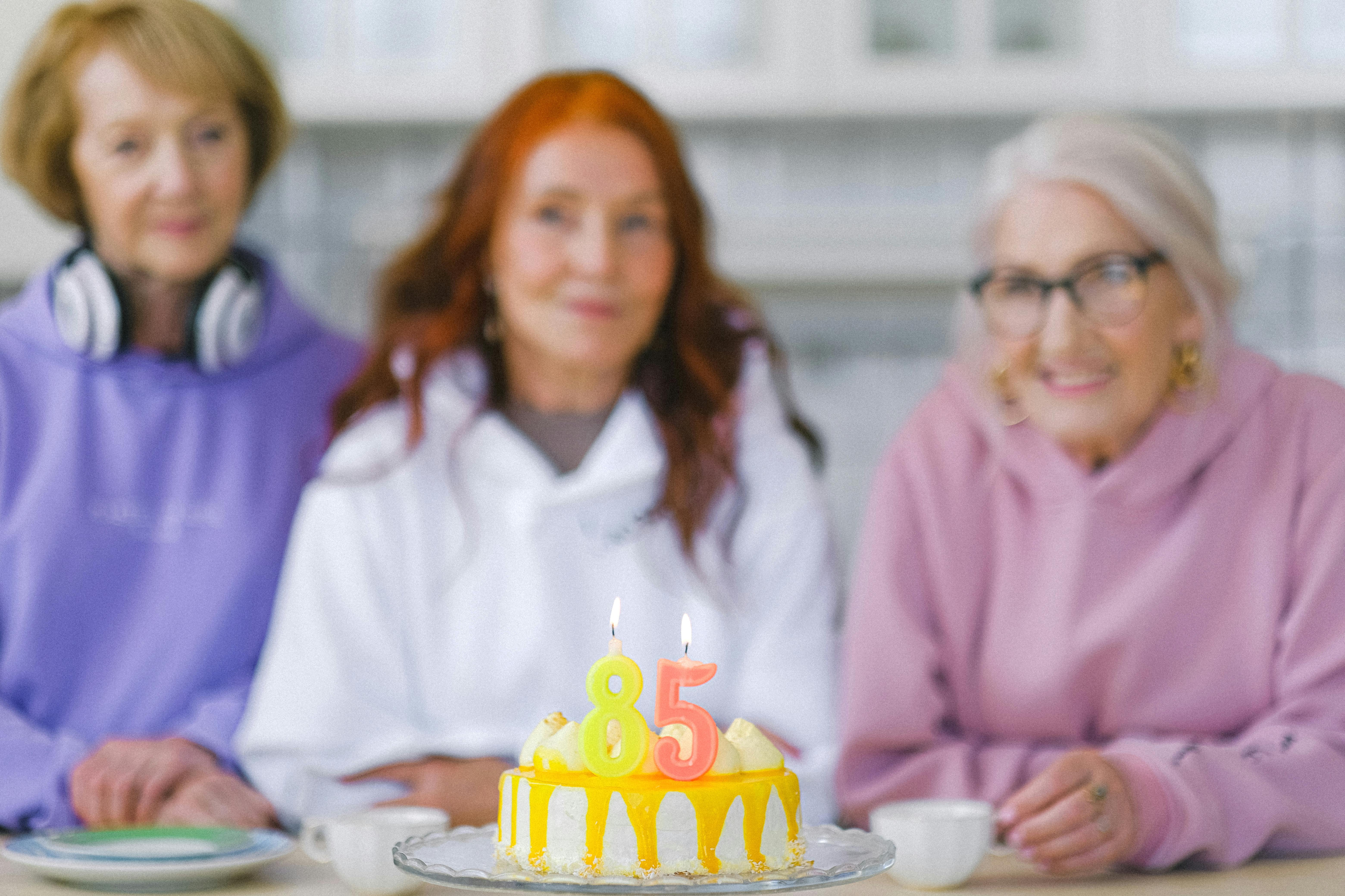 Birthday cake against blurred senior women in light room · Free Stock Photo