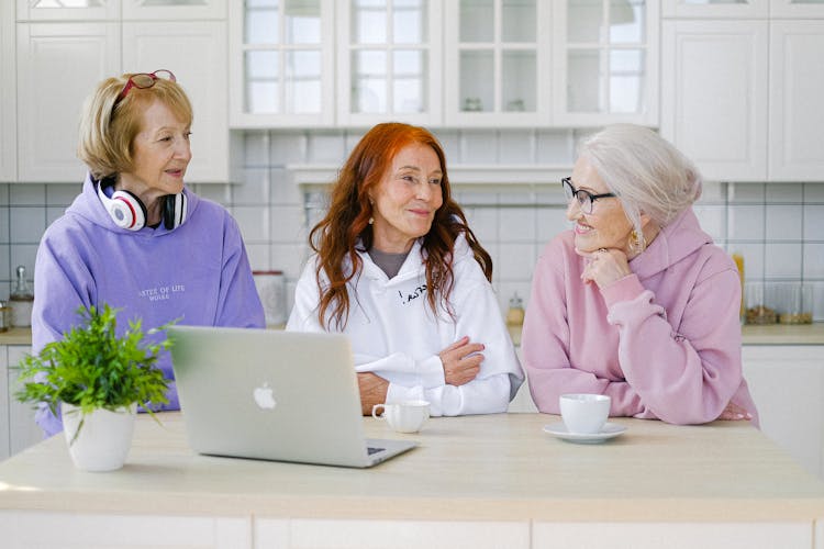 Cheerful Aged Women Friends Communicating While Sitting At Table At Home