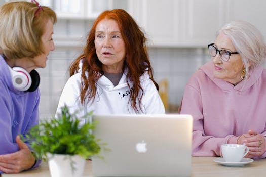 Three senior women chatting with a laptop and cup of tea, embracing technology indoors.