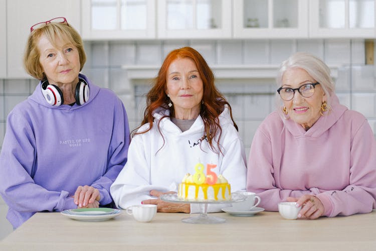 Senior Women Friends Sitting At Table With Birthday Cake