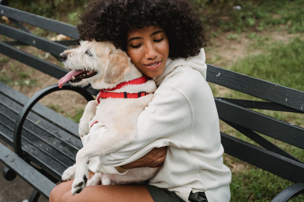 A woman hugging her dog on a park bench