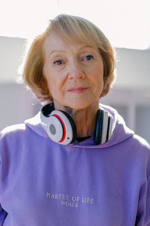 Modern blonde short haired elderly woman in hoodie with headphones looking at camera thoughtfully