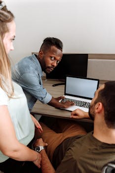 A diverse group of adults discussing in an office setting with a laptop.