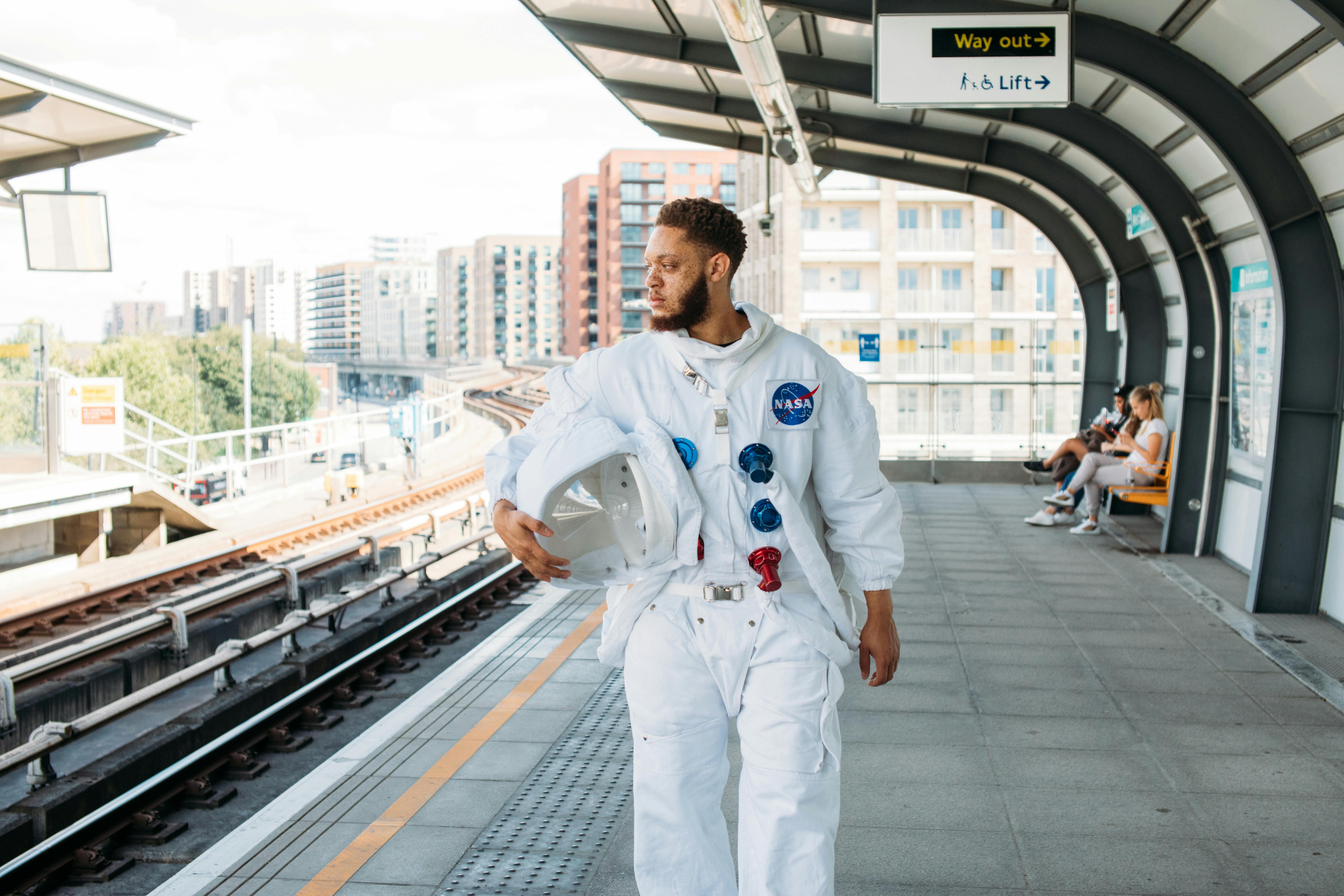 一名身着宇航服的男子在城市火车站手持头盔，将太空主题与城市生活融为一体
