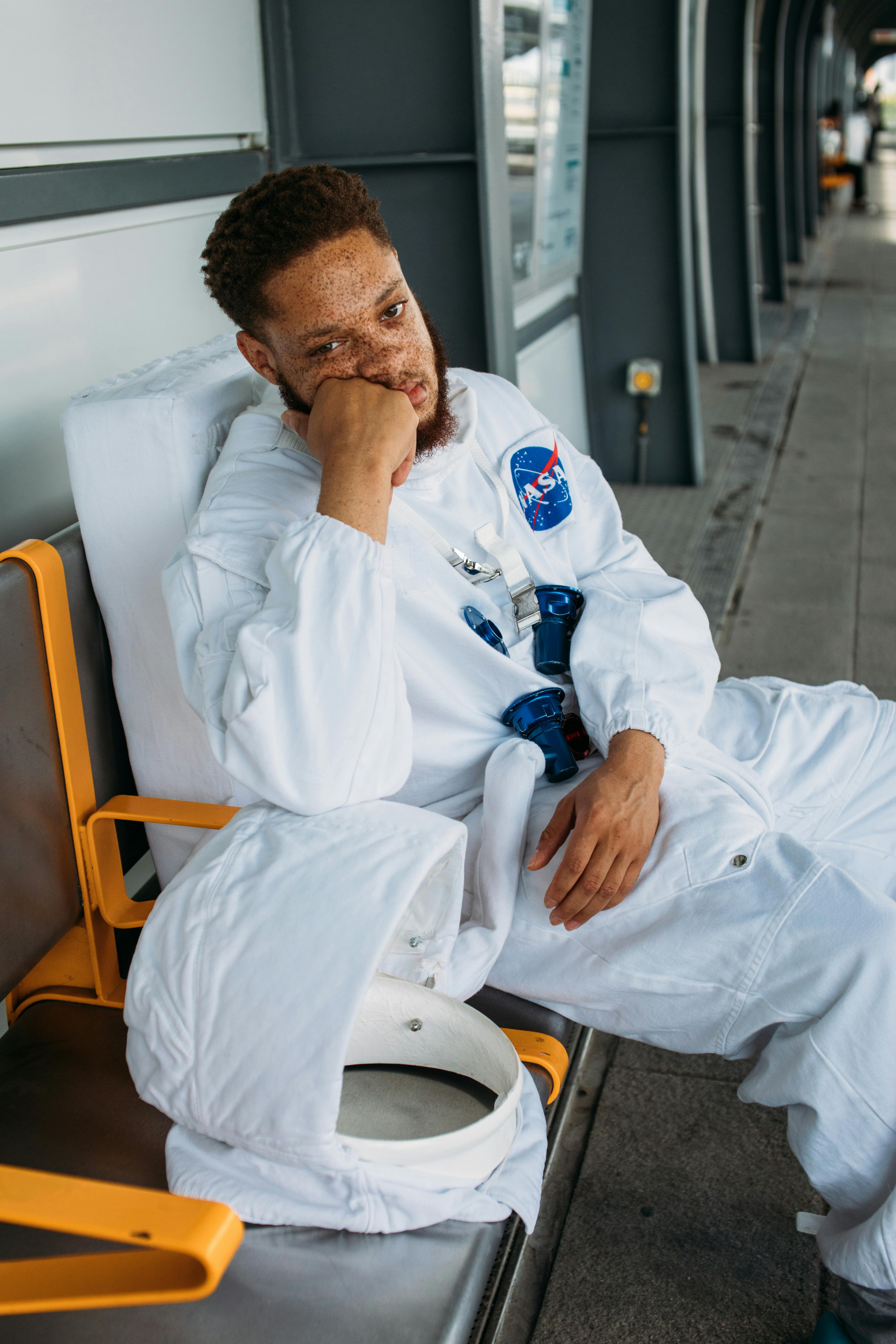 一个穿着太空服的男人坐在公共交通区，看起来很无聊