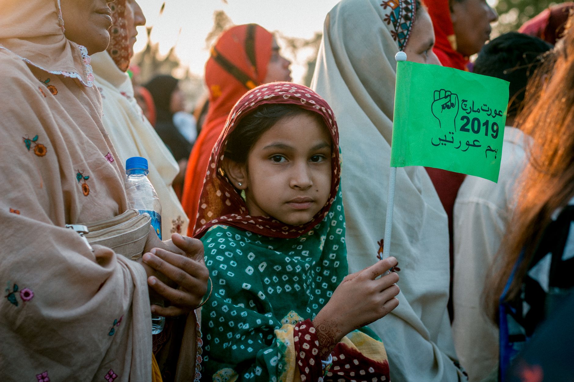 Young Pakistani girl at a women's rights demonstration holding a protest flag, promoting unity and feminism.
