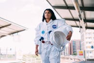 一名身穿白色太空服的妇女手持头盔，站在郊区火车站的站台上