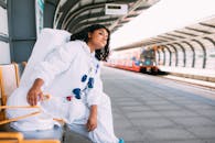 一名身着太空服的女人坐在现代火车站的长椅上，等待火车到来