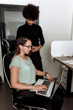 Two professionals collaborating on a project using a laptop in a modern office environment.