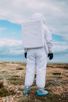 在蓝色多云的天空下，一个穿着白色太空服的人站在户外，面对开阔的土地