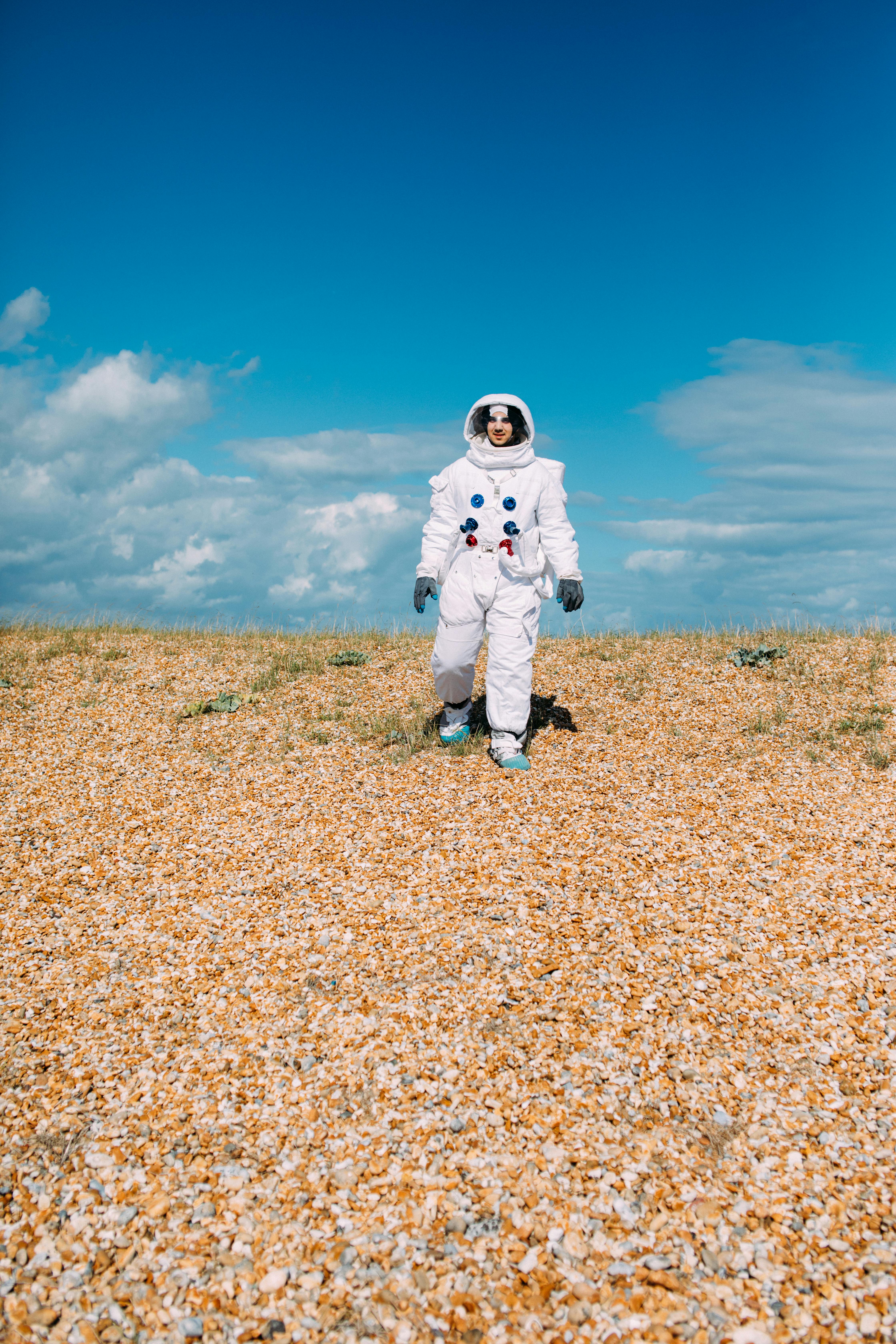 穿着太空服的人行走在晴朗蓝天下岩石遍布的户外地形上