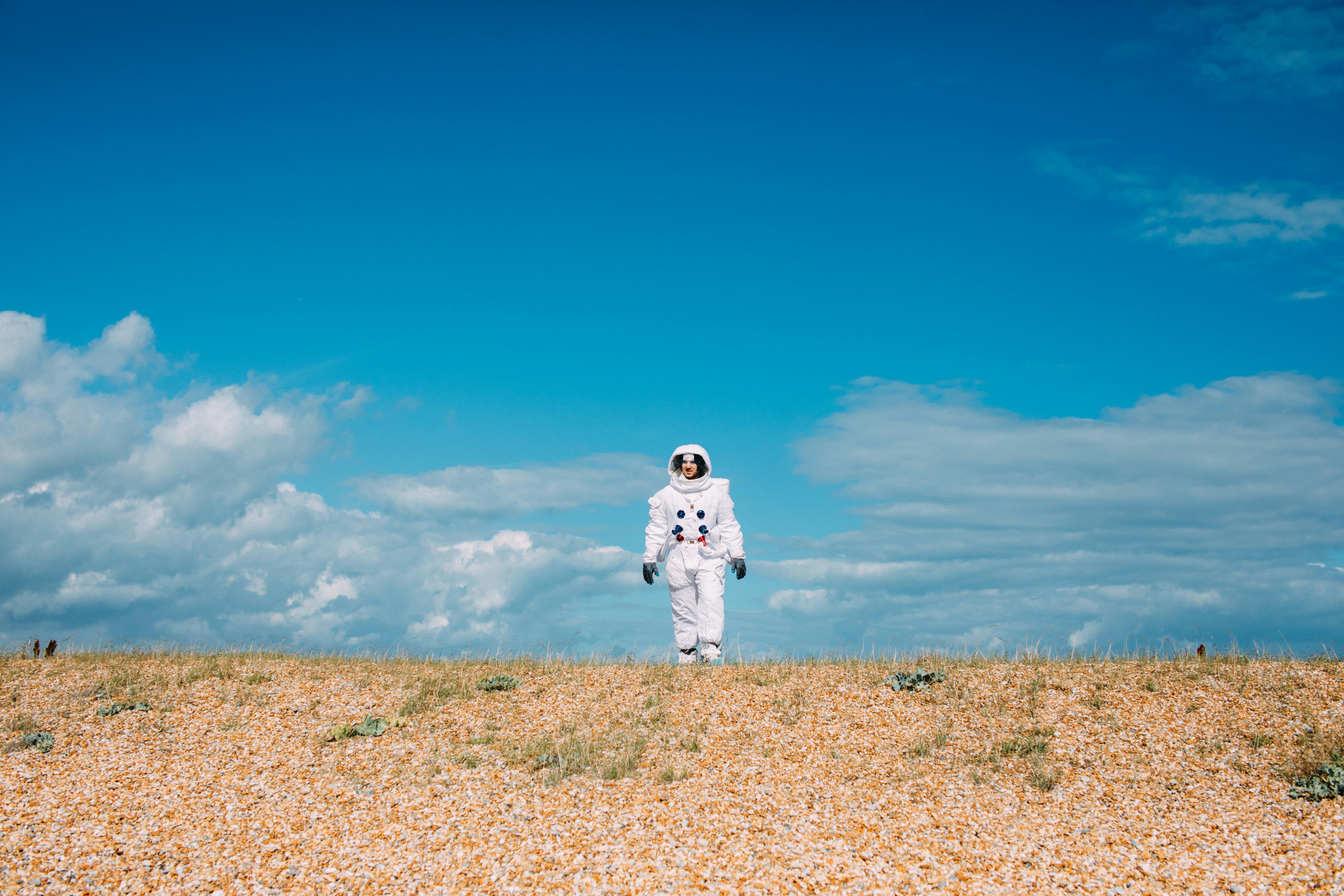 在充满活力的蓝天下，一位穿着宇航服的宇航员正穿越贫瘠的沙漠