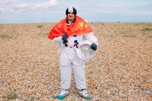 一名男子身穿太空服，手持头盔和红旗，站在岩石地形上