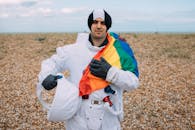 在鹅卵石海滩上，一个穿着太空服的人举着彩虹骄傲旗