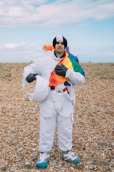 一个穿着太空服的成年人，在晴朗的天空下，举着五颜六色的旗帜站在鹅卵石景观上