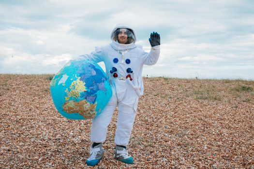 一个穿着太空服的男人在户外的岩石海滩上拿着一个地球仪