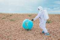 在多云的天空下，一个穿着宇航员服装的人正在鹅卵石场地上与地球仪互动