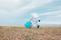 宇航员穿着太空服，走在鹅卵石铺就的海滩上，上面放着一个可充气的地球仪