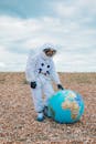 一名宇航员穿着太空服，站在鹅卵石海滩上的充气地球仪旁边