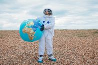 穿着太空服的宇航员在户外岩石地形上拿着一个大型地球