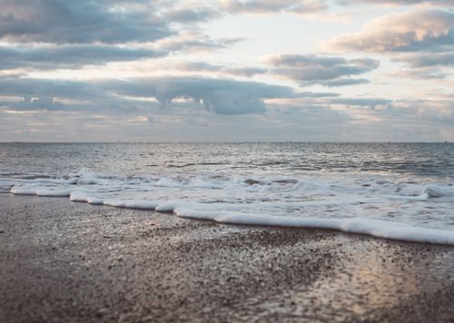 Free Ground level of wavy ocean with ripples on sandy shore under cloudy sky at sunset Stock Photo