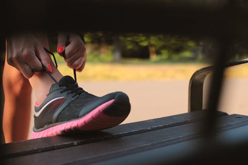 Free Woman in Black and Pink Sneaker Tying Lace of Her Shoe Stock Photo