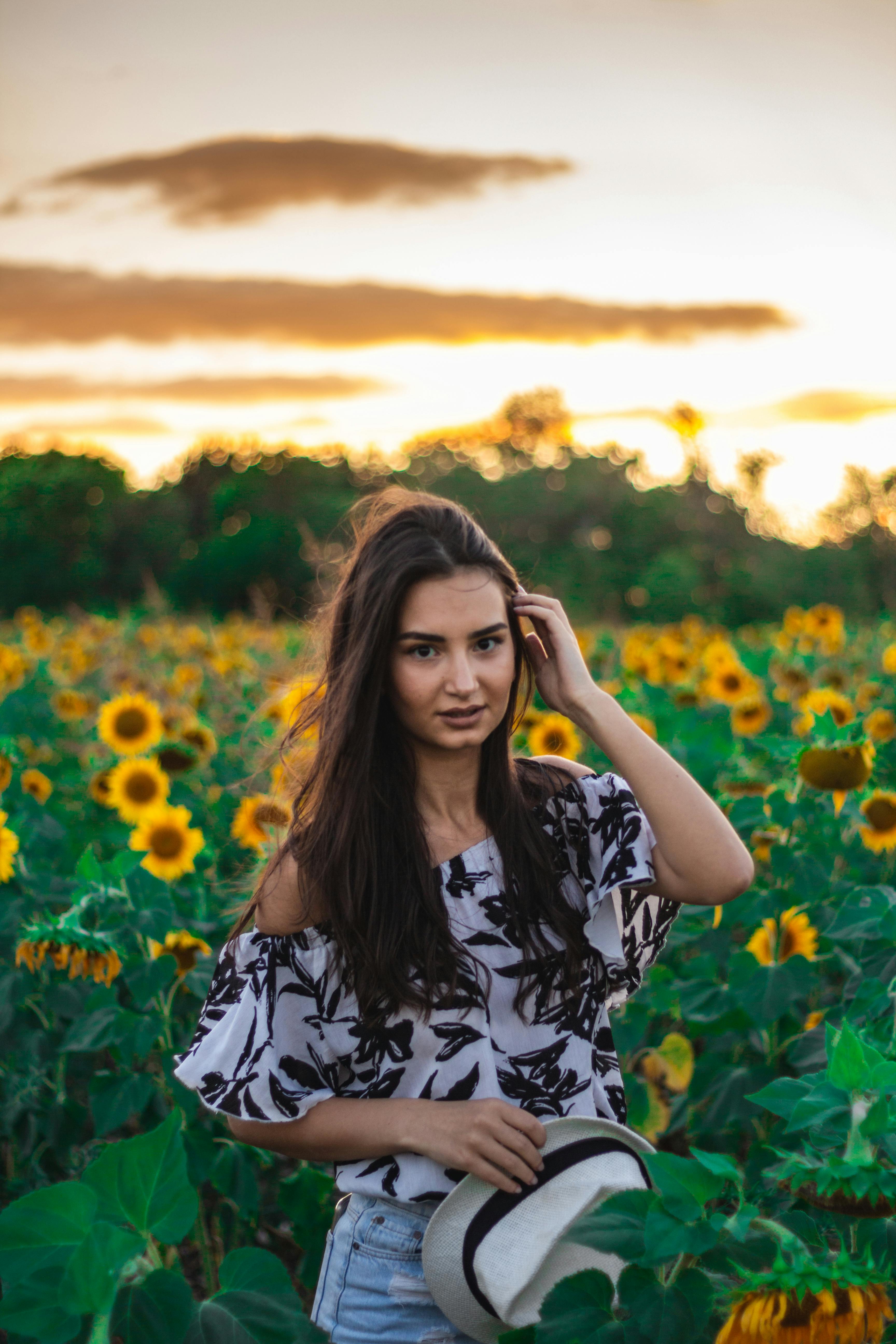 A Woman Holding a Sun Hat and Stem of Sunflower Standing in Front of ...