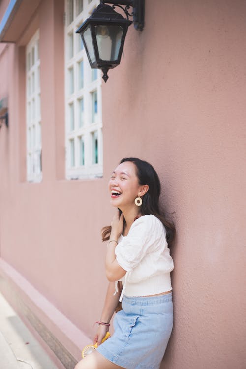 Young Asian woman laughing happily while leaning on wall