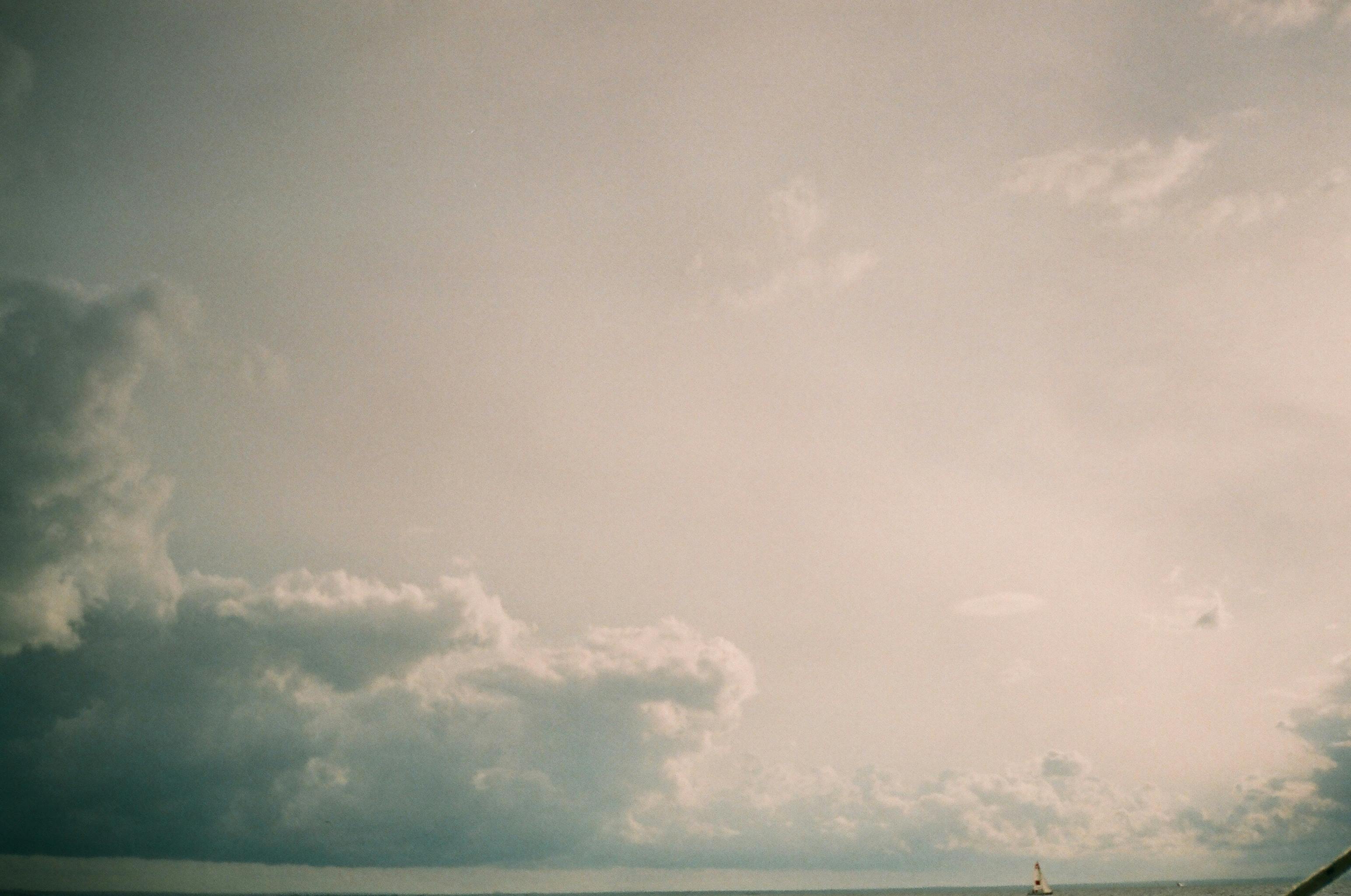 A tranquil sky filled with clouds over an ocean horizon, featuring a solitary sailboat.