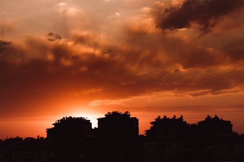 Silhouette of Buildings and Trees under Dramatic Sky at Sunset 