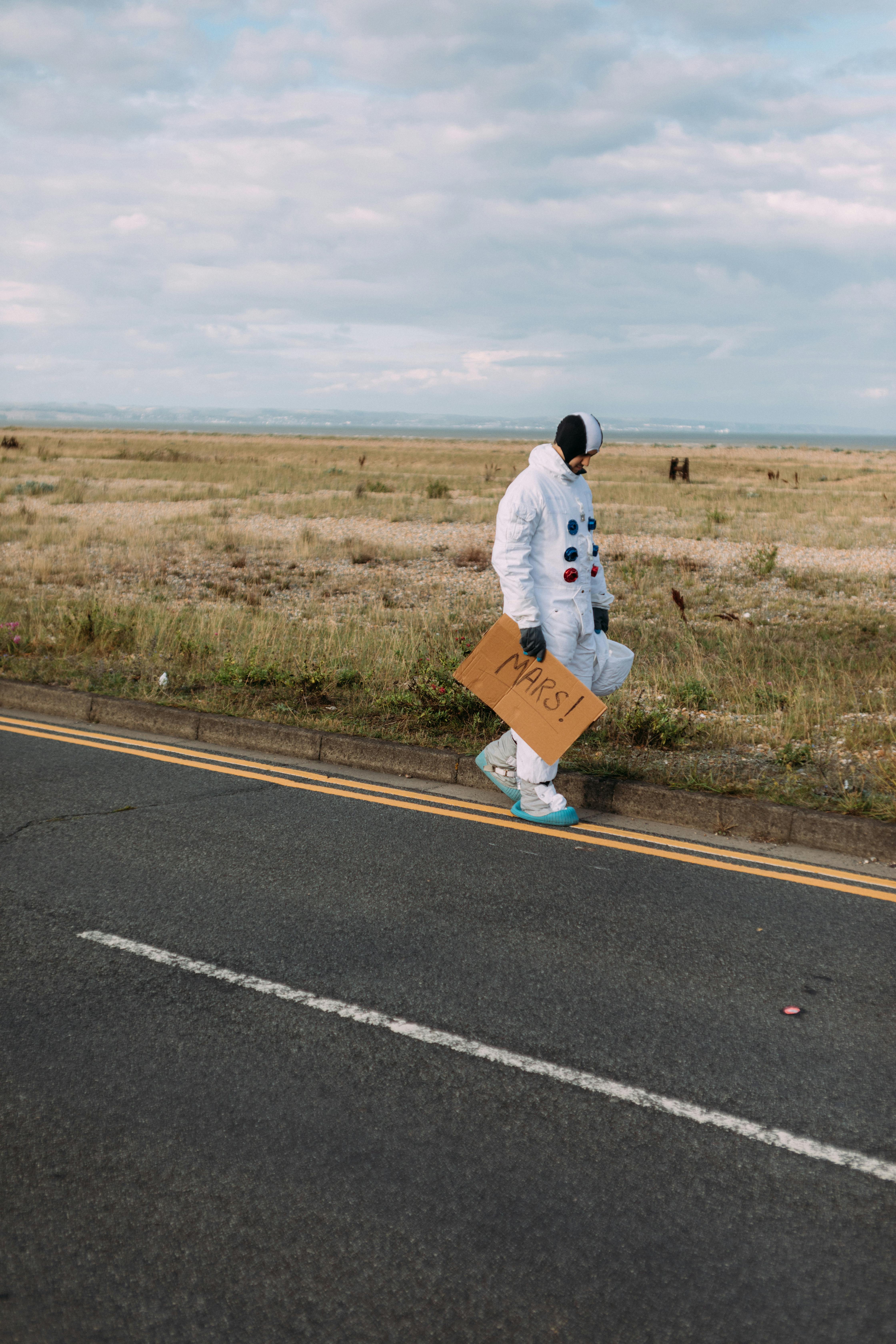 一个穿着宇航服的人举着火星标志走在乡村路边