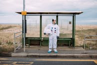 一名身着宇航服的人正在乡村公交站等车，营造出异想天开又超现实的场景