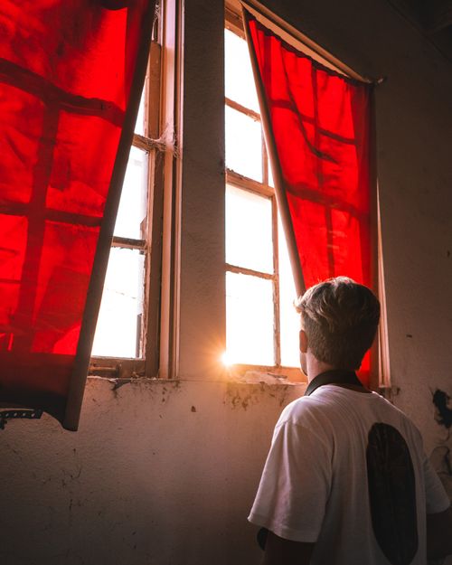 Free Back view of unrecognizable male standing in room with bright sunlight shining through window in abandoned building Stock Photo