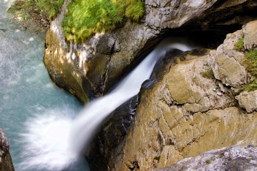 From above long exposure of fast foaming cascade falling from wet rocky cliff covered with moss in ravine in nature