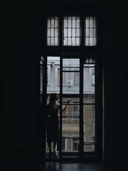 一名妇女站在一扇情绪多变的大窗户旁，向外眺望城市建筑