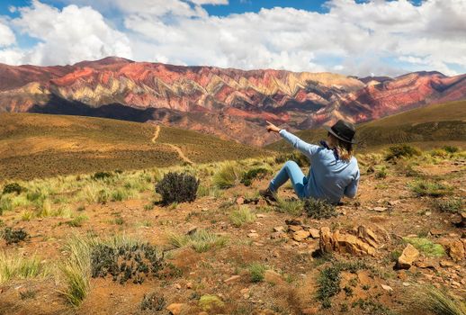 A woman in a hat admires the vibrant mountain landscape under a blue sky.