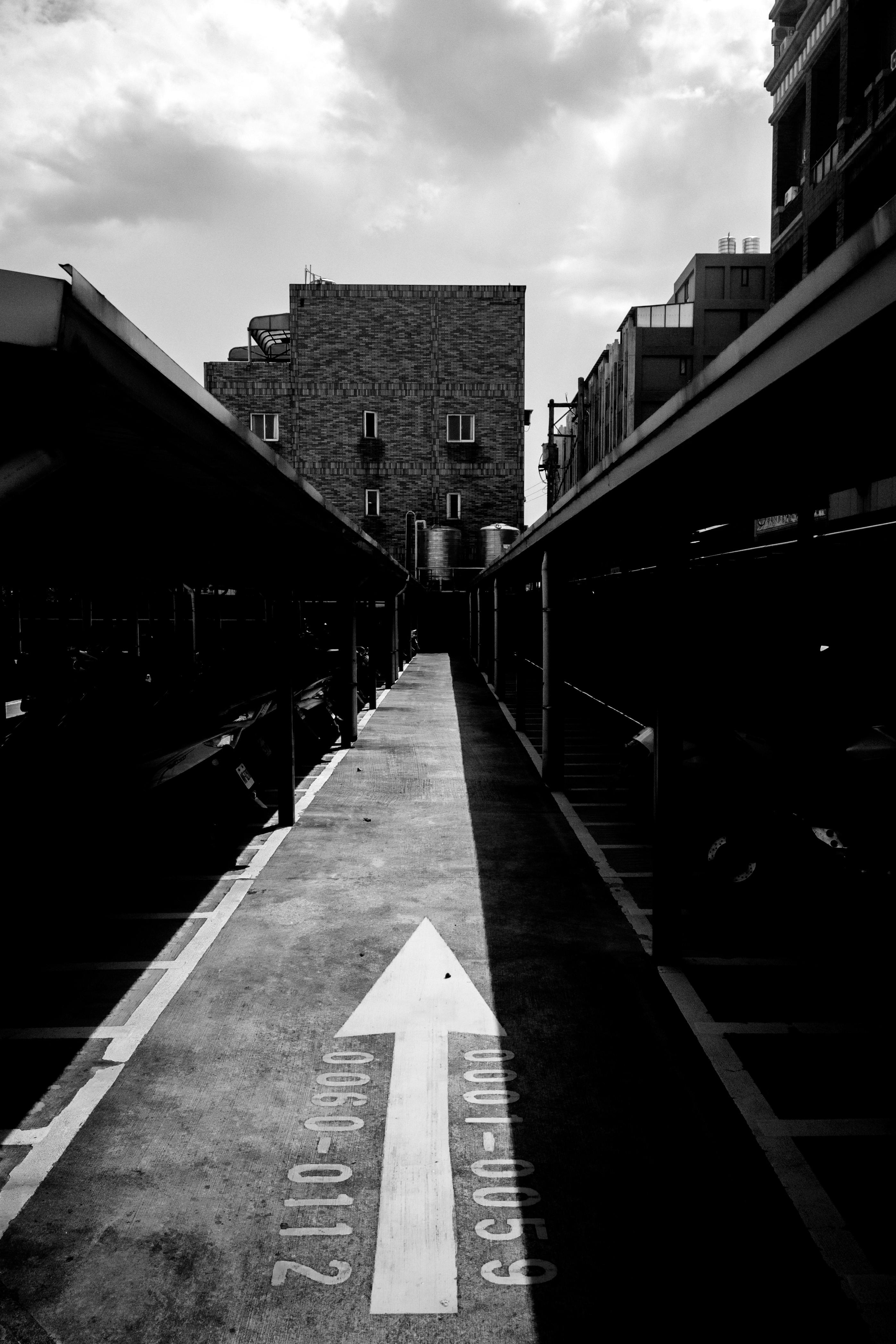 Black and white image of a parking area with an arrow, emphasizing shadows and architecture.