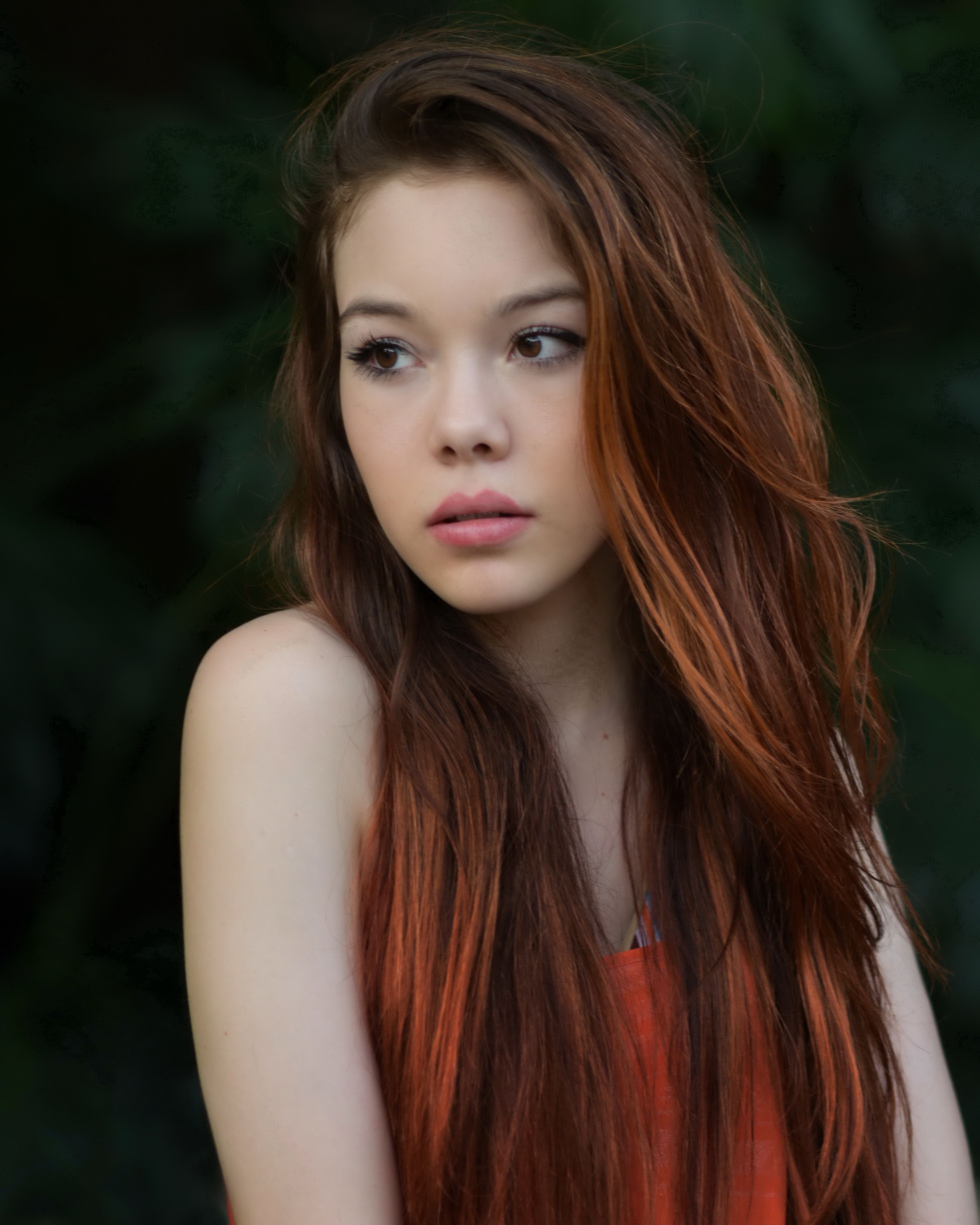 Elegant portrait of a woman with long auburn hair in a natural outdoor setting.