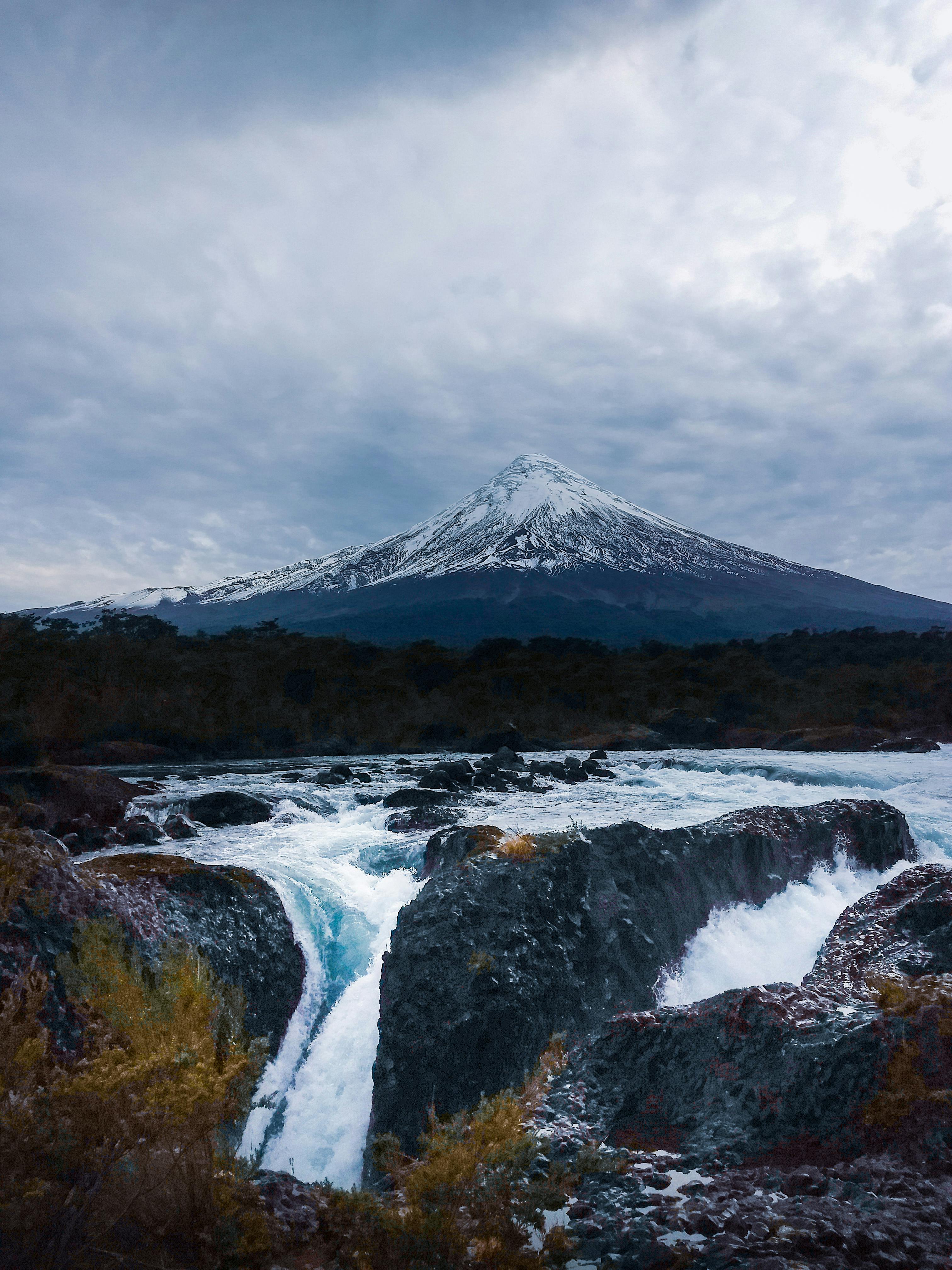 阴沉的天空下，前景是急流，远处是令人惊叹的雪山景色