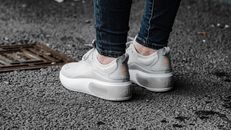 Feet of faceless person wearing jeans and white sneakers standing on messy asphalt pavement near stormwater runoff