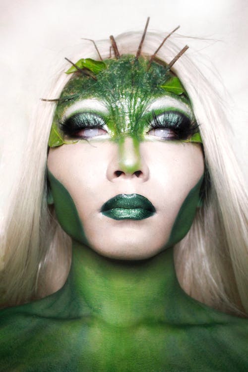 Trans model covered with green paint and creative stylish Halloween makeup representing mysterious character against white background