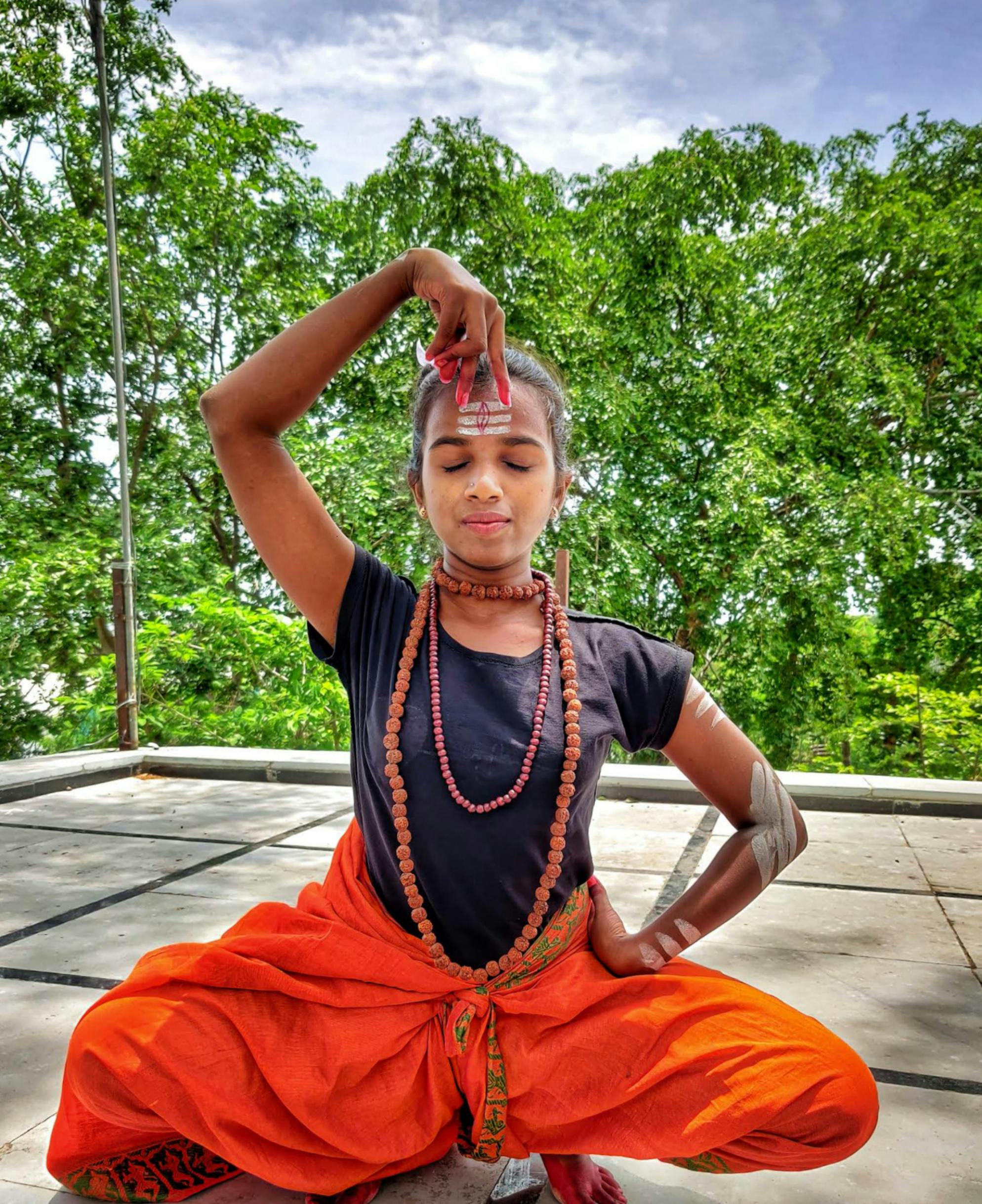 Woman performs yoga meditation with serene expression amidst lush greenery.